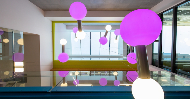 Light fittings with pink and white bulbs on brass tubing representing molecules light a ceiling space