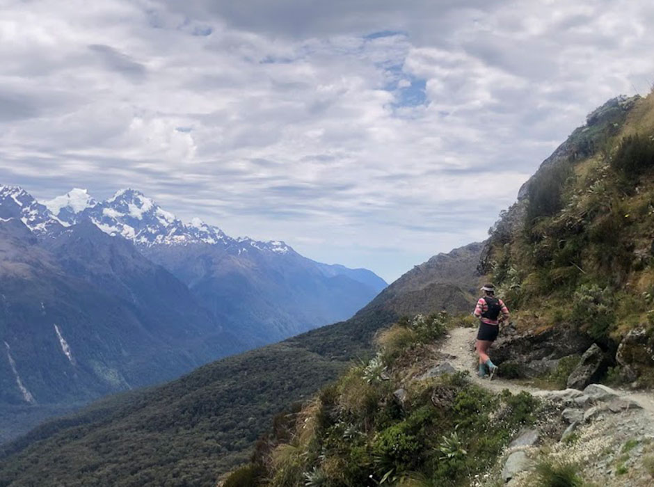 a woman running along a trail on a mountain 
