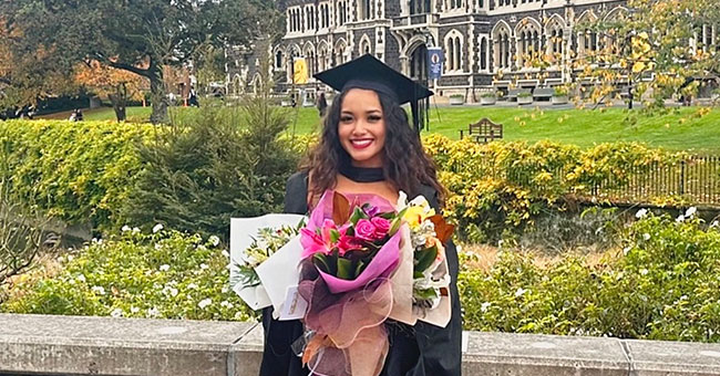 A woman dressed in graduation robes is pictured in front of the Clocktower.