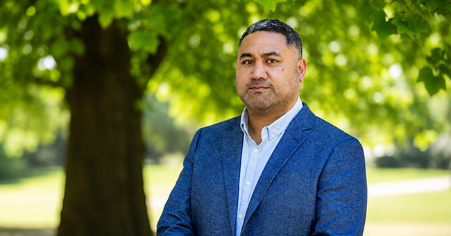 A man in a blue suit is pictured outside in front of a tree.
