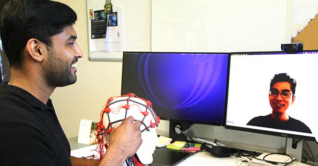 A man seated in front of a computer, chatting to a person via the computer with the person's face on screen