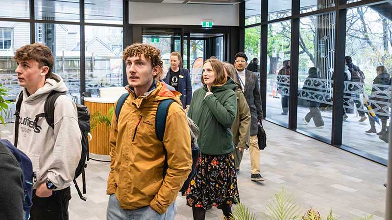 People arriving through a glass door in a foyer to look through a building 