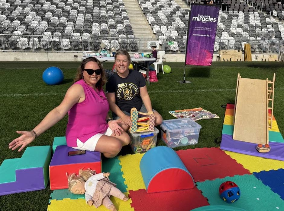 Two women are pictured sitting on a blanket at a stadium.