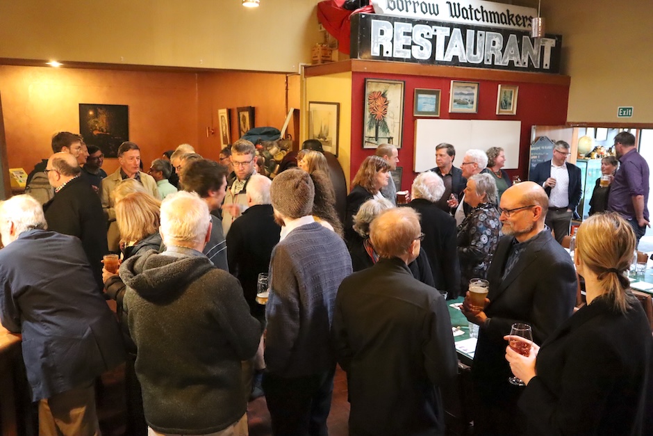 A crowd of people with drinks, standing and talking to each other.