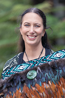Photograph of Professor Jacinta Ruru wearing a feathered korowai, smiling to camera