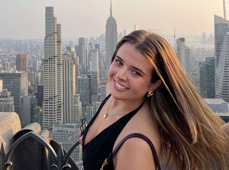 A woman standing atop a building with the new york skyline in the background 