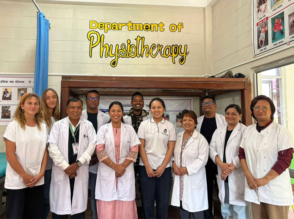 Two rows of people standing beneath a sign that says department of physiotherapy, some of the people are wearing white coats