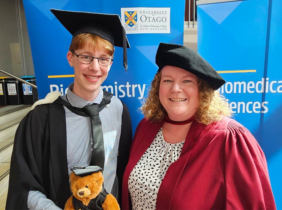 A student in graduation regalia standing next to a woman in a graduation regalia