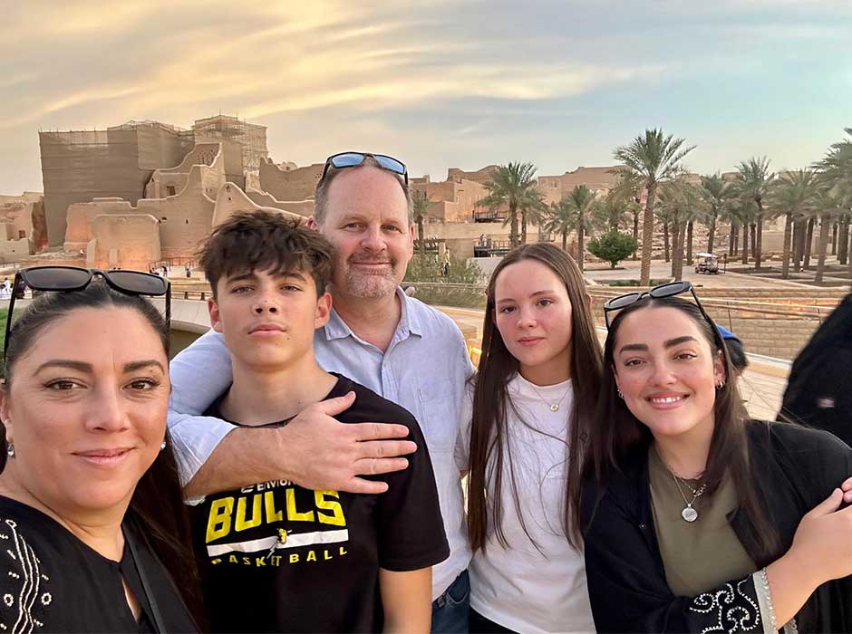 A family of five standing in front of buildings and palm trees