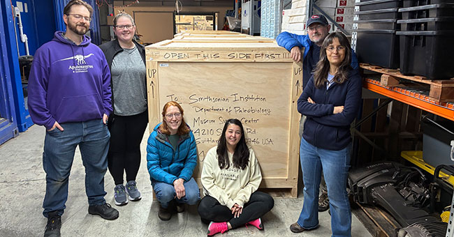 A group of people pose with a large wooden box.