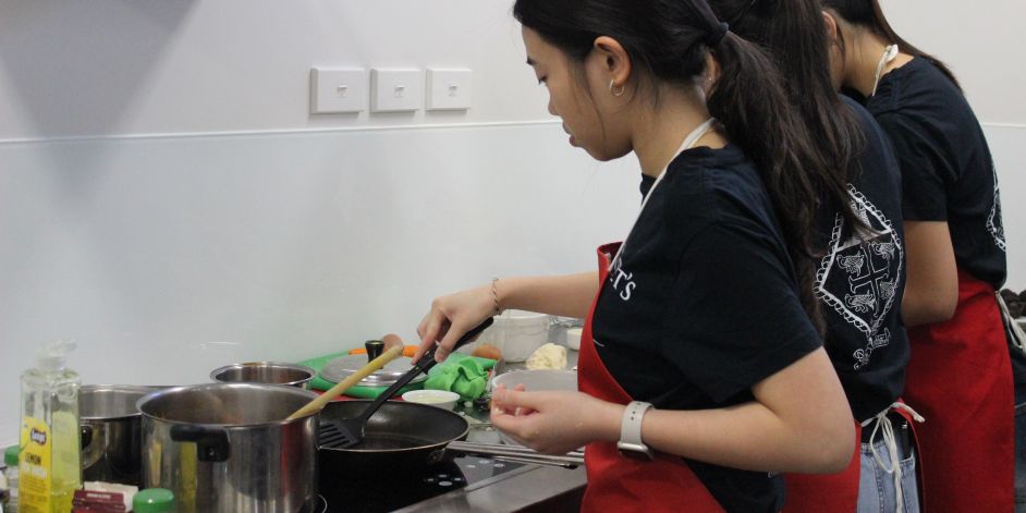 Three students from St Margaret's College wearing aprons and cooking in a competition