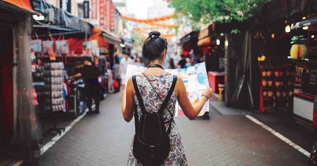 Young woman with a backpack and holding a map walking down an Asian market street.