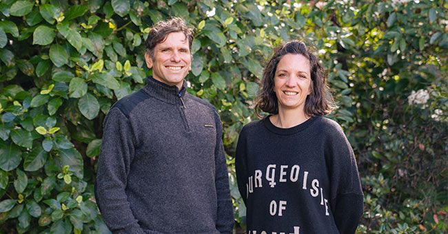A man and a woman pose for a photo with trees in the background.