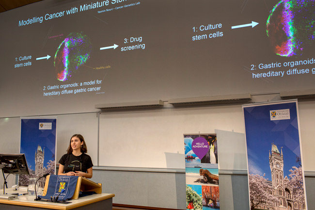 Master's student Yasmin Nouri talks about her research in front of a picture of stem cell organoids