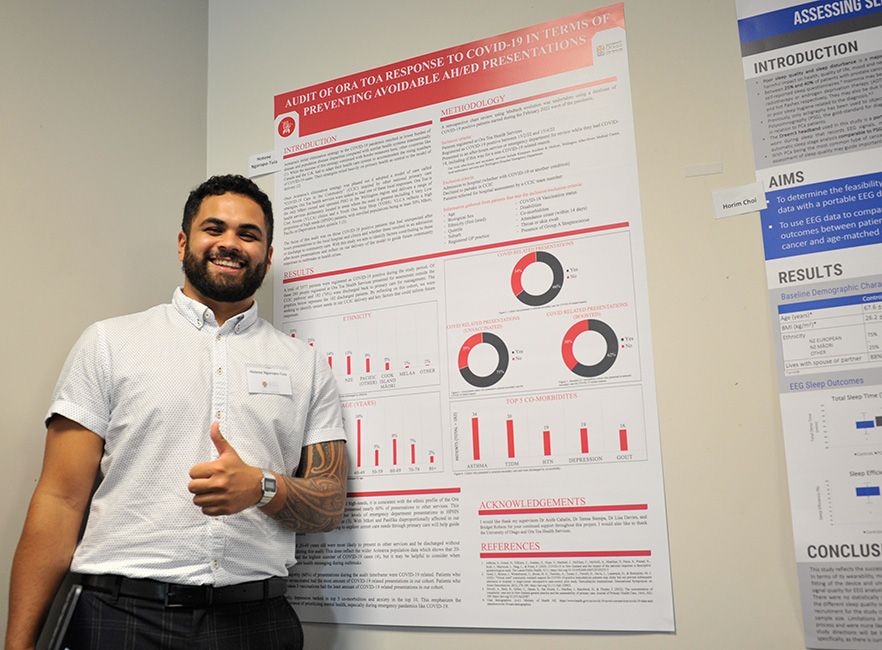 Summer students 2023 winner Hotene Ngaropo-Tuia standing in front of his poster image