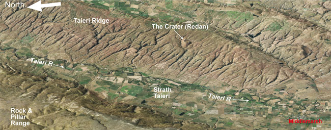 Oblique view of the Strath Taieri basin and Middlemarch township, between two actively rising schist ridges: Rock & Pillar Range and Taieri Ridge. The Otago Central Rail Trail runs parallel to the Taieri River on the western side of the valley, northwards from Middlemarch. The Crater (also called Redan) on Taieri Ridge was formed by an explosive volcanic eruption 25 million years ago, when the land was near to sea level. The crater rim is defined by fragmental schist and volcanic material blown out of the eruption cavity.
