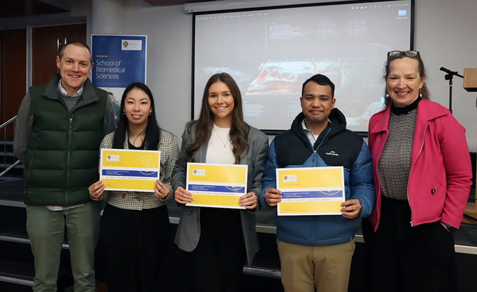 Three students: Samantha Nie, Geogia Keelty, and Tristan Paulino holding their certificates, with Peter Mace and Lisa Matisoo-Smith on either flank.
