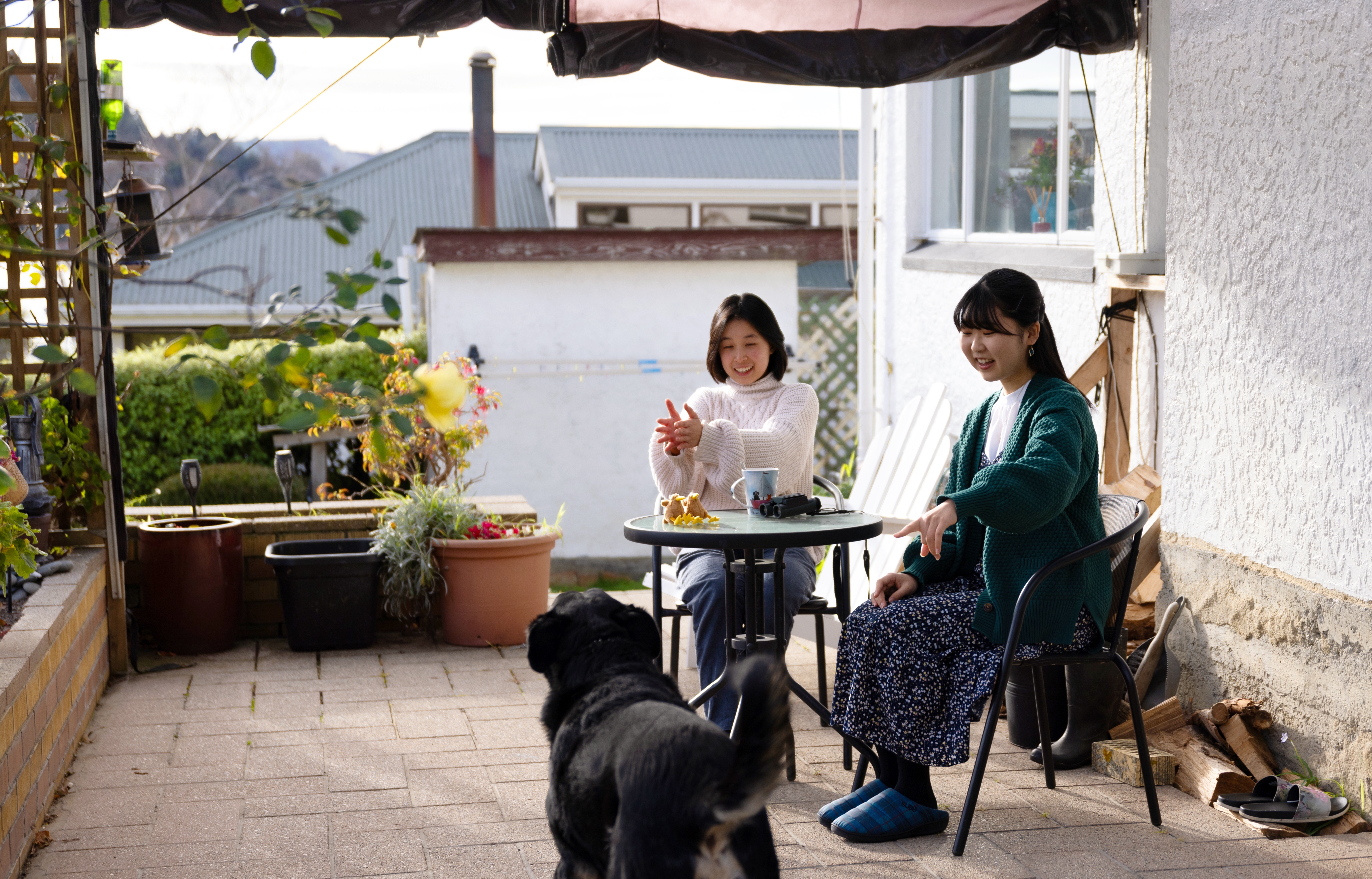 Two exchange students sitting outside on a verardah with a big black dog.