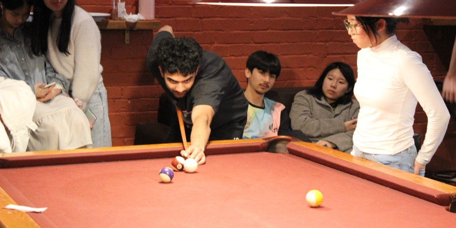 Guy leaning across a terracotta-coloured table to play a pool shot.