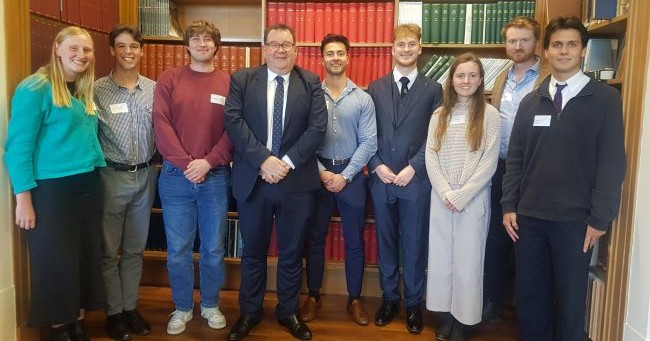 A row of people standing in front of a book case 