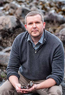 Dr Nathan Kenny holds mussels on a rocky shore