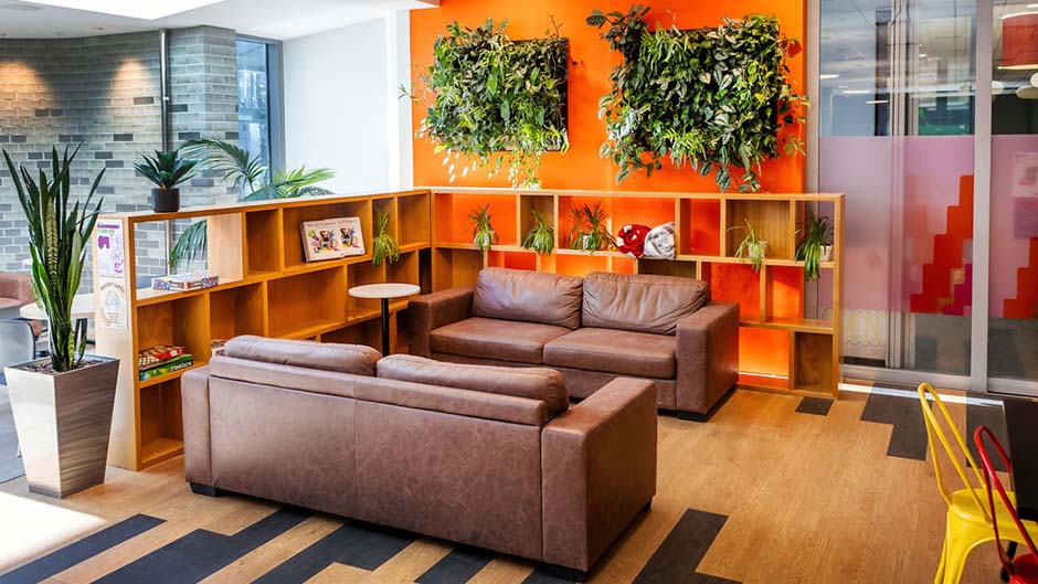 Two couches and some shelves with games and pot plants in the corner of Auahi Ora café