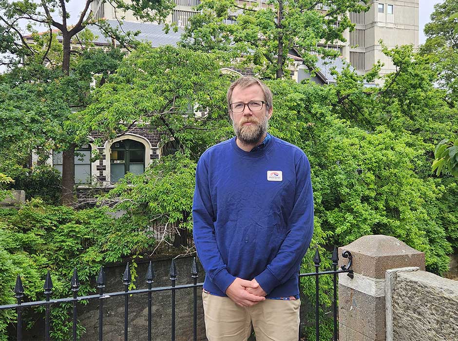 A man standing in front of railing with trees behind him