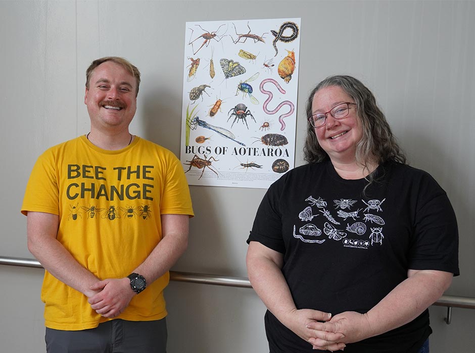 Man in yellow tee and woman in black tee standing in front of a poster of bugs