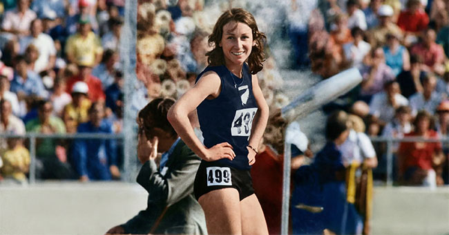 An older photo of a female athlete, wearing a New Zealand sports kit, standing in front of a crowd.