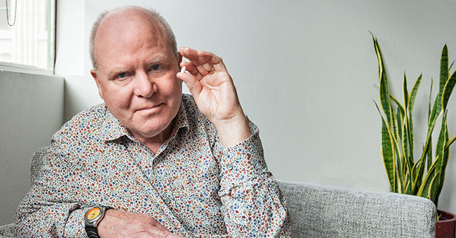A man sitting on a couch holds up a white pill.