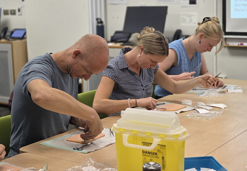 Three students practise their suturing skills on soft plastic in a classroom setting