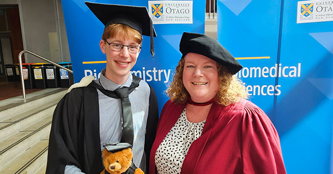 A student in graduation regalia standing next to a woman in a graduation regalia