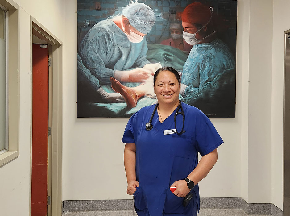 A female doctor standing in front of a painting of two doctors operating. 
