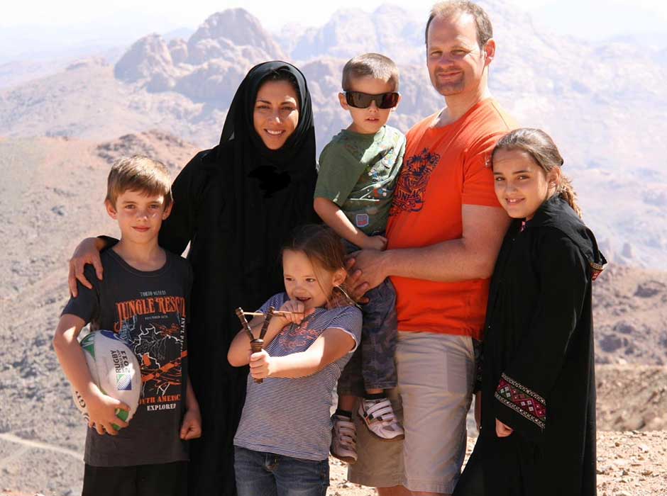 A family of five standing in front of a rocky, sandy landscape