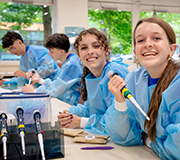 Four students wearing protective gowns use Genetics testing equipment in a lab sitting.