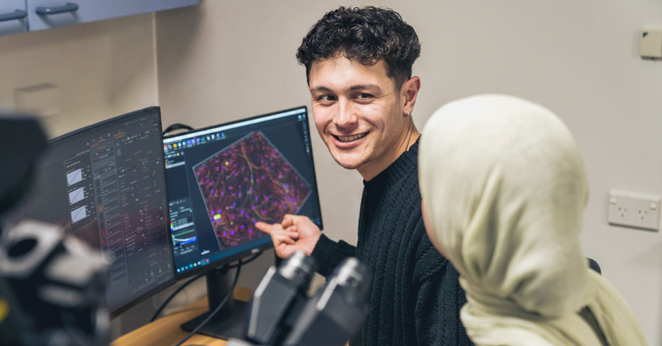 Young man pointing to a computer screen displaying a detailed medical scan and turning to regard a woman in headscarf.