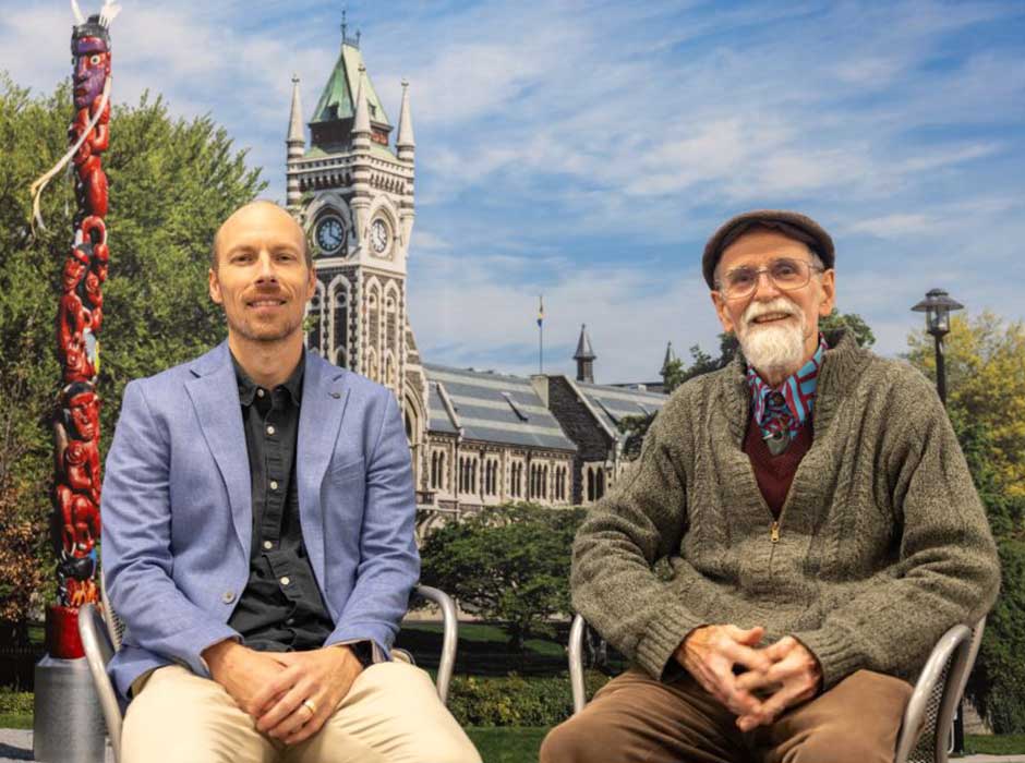 two men seated in front of an image of the University clocktower and Pou