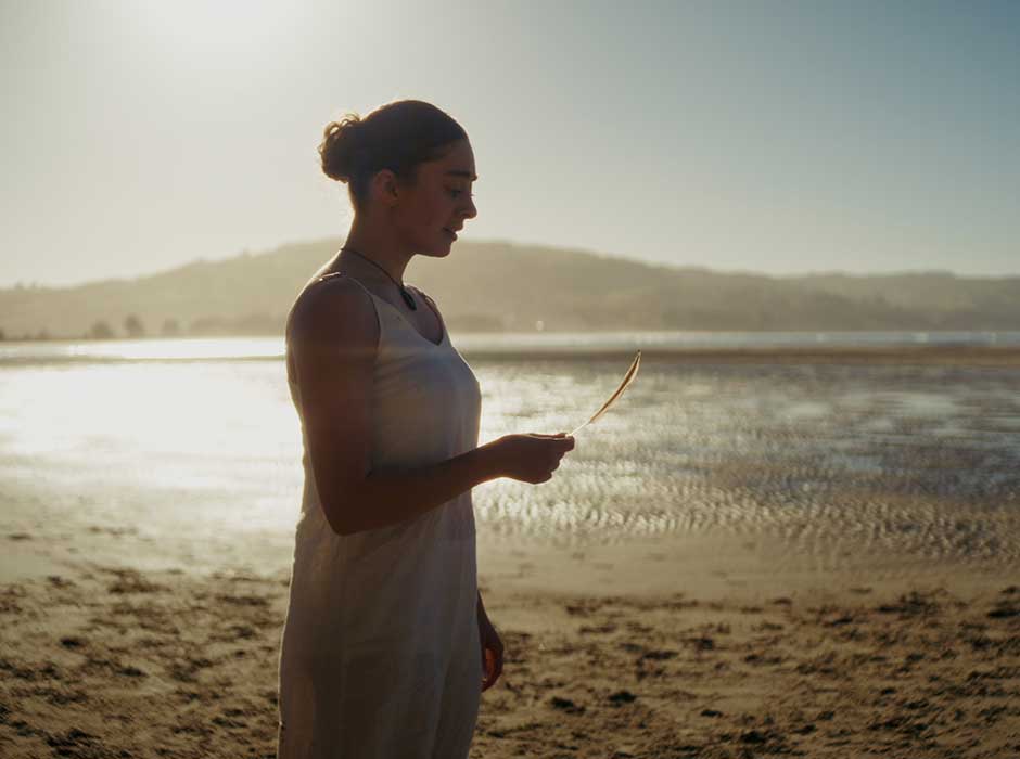 A woman stands on a beach holding a feather