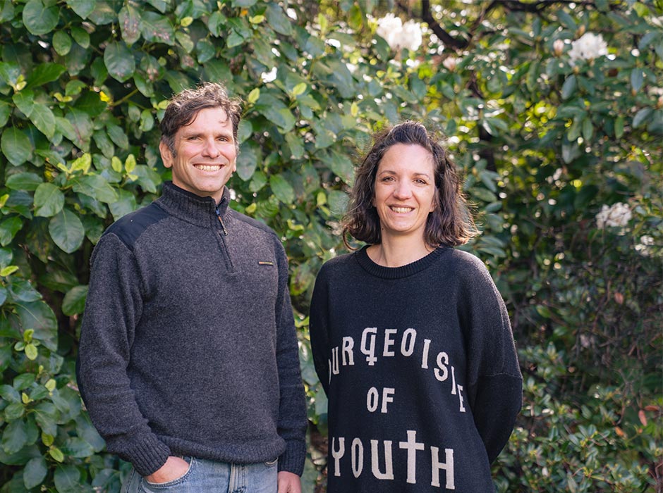 A man and a woman pose for a photo with trees in the background.