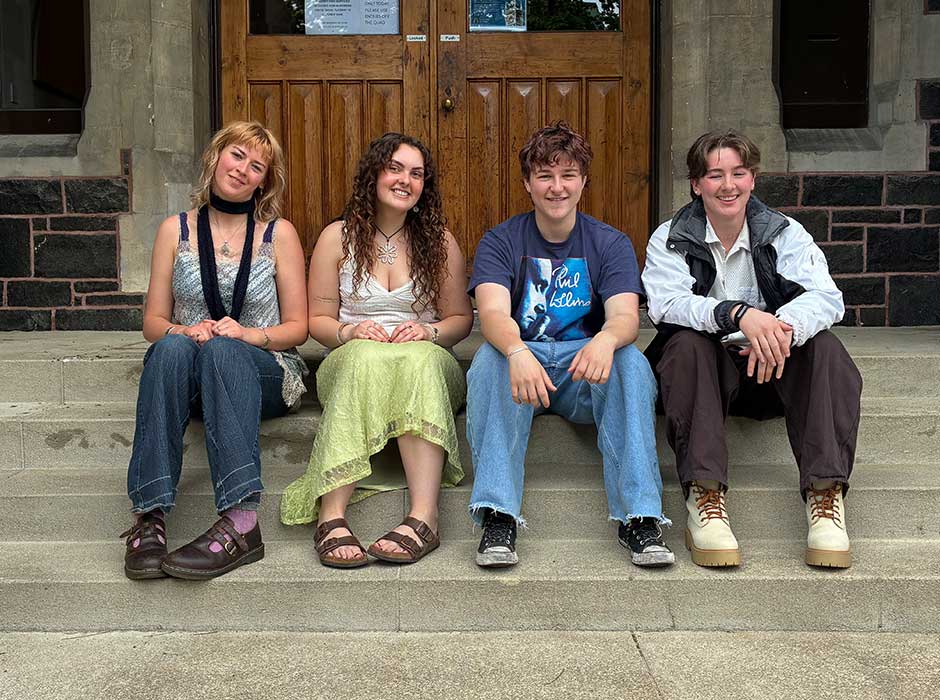 four young people seated on steps at the front of the Clocktower building 