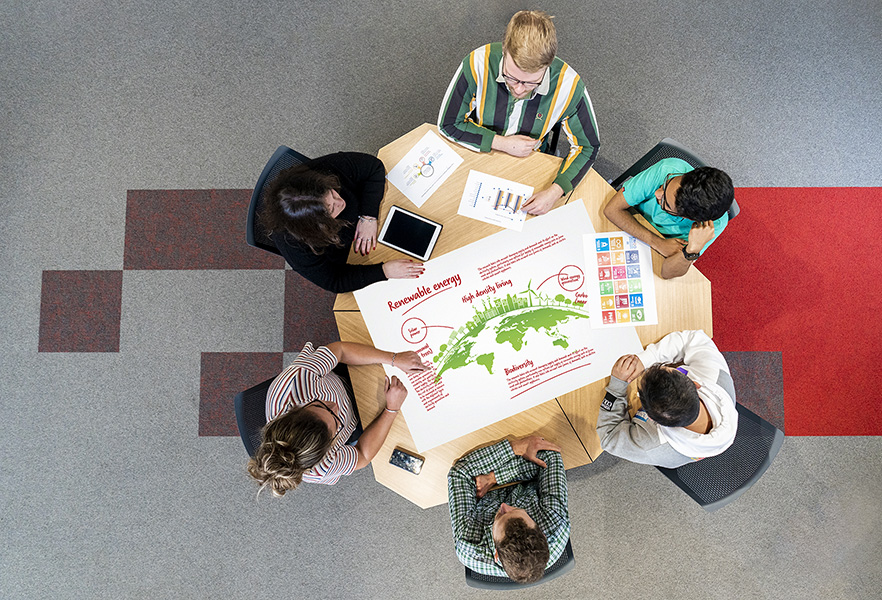 Aerial view of 6 students at a table looking at sustainablility artwork image 1x