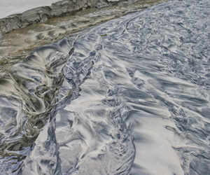 Erosion at work! Artful patterns in beach sand created by a fresh water stream cutting a channel into the sand and forming meandering stream patterns running seawards