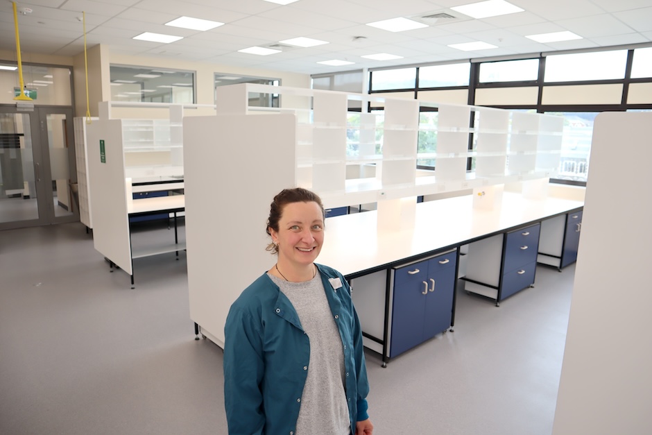 A researcher wearing a blue lab coat stands in a clean new empty research laboratory
