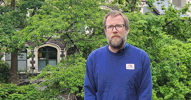 A man standing in front of railing with trees behind him