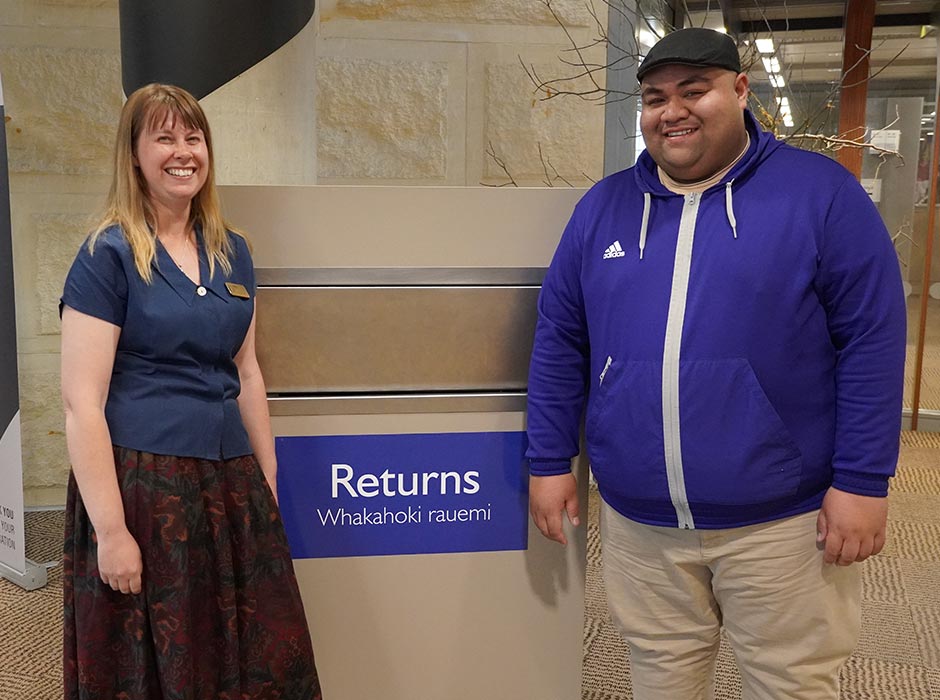 A female staff member and a male student look happy by the Returns bin at Central Library.