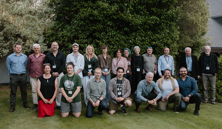 Two rows of smiling people, the front one with people kneeling or crouching, the back row standing, all on a lawn with trees in the background