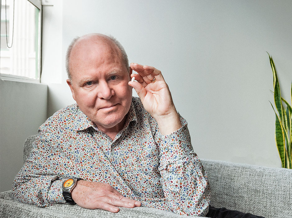 A man sitting on a couch holds up a white pill.