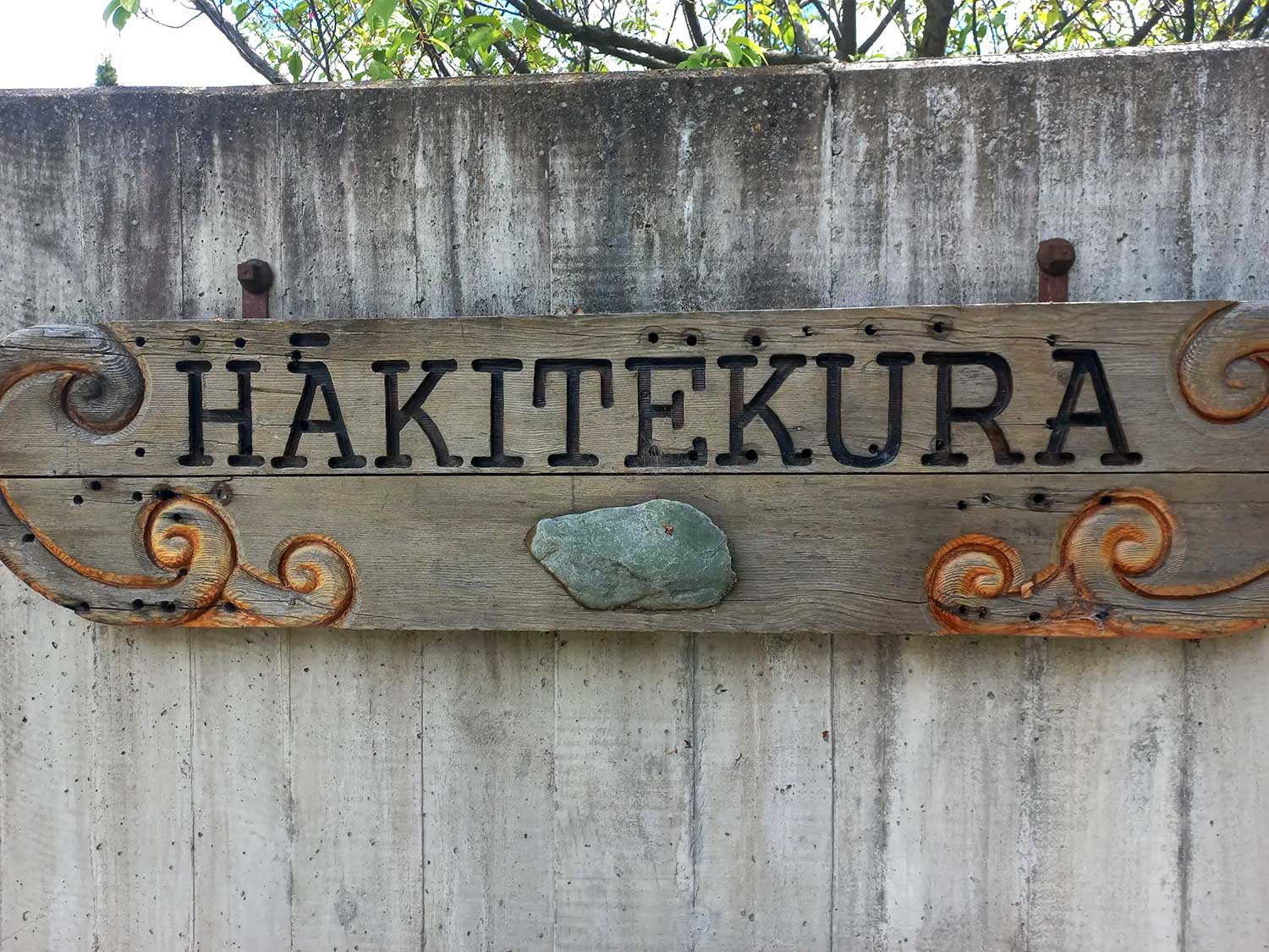 Hākitekura wooden sign with inlaid koru and pounamu