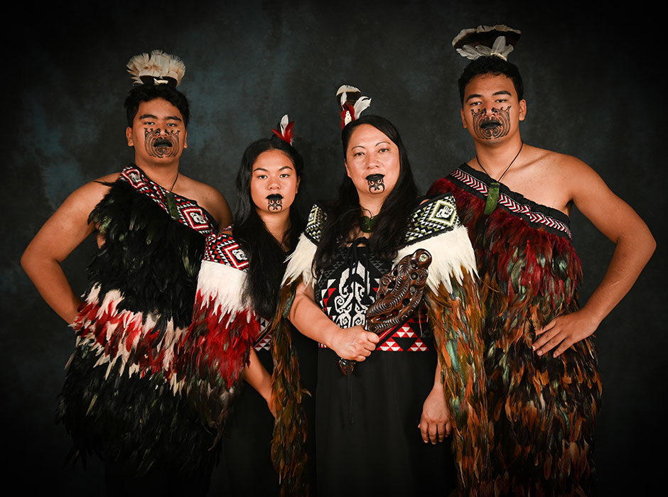 A Māori woman and her three children posing for a family portrait dressed in traditional Māori attire