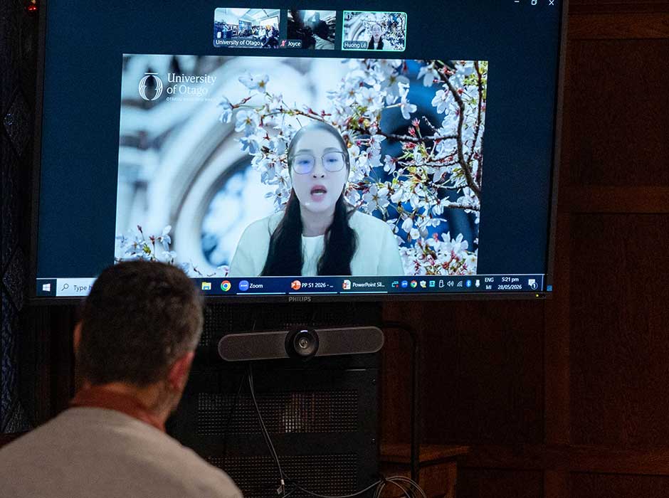 A woman speaking on a digital screen to a room